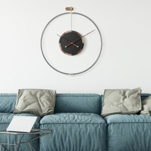 Horloge nordique noire installée sur un mur beige au-dessus d'un canapé bleu avec des coussins gris
