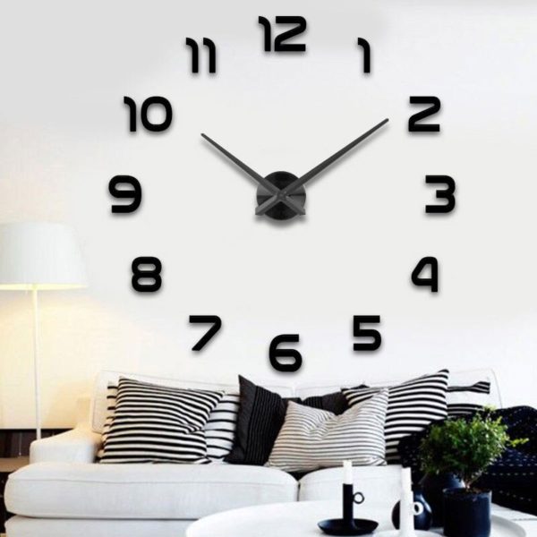 Grande horloge sticker noire installée dans un salon au-dessus d'un canapé noir et blanc