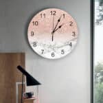 installée sur un mur gris , une horloge ronde, rose et blanche pailleté à aiguilles