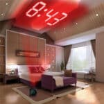 dans une chambre un réveil avec un affichage par projecteur est posé au sol près du lit et projette l'heure au plafond en rouge