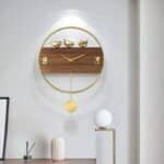 horloge ronde dorée avec pendule et centre bois avec 3 oiseaux en 3D , installée sur un mur noir au dessus d'un canapé marron