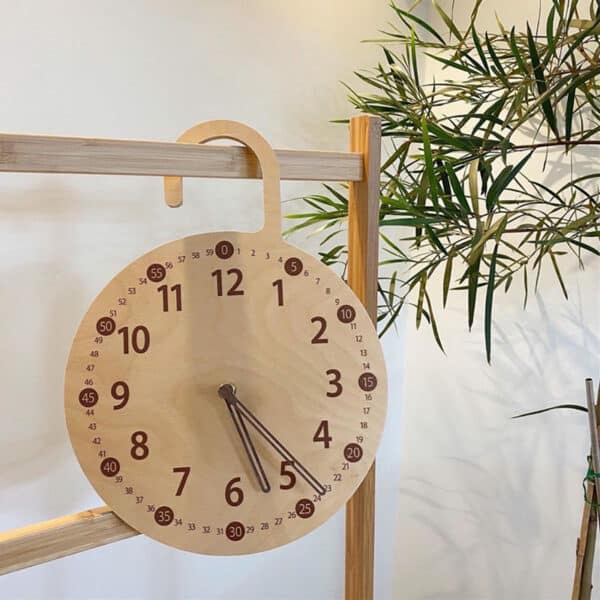 Horloge murale nordique en bois suspendue style cadenas ouvert suspendu à un portant en bois près d'une plante