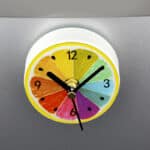 Horloge murale petite et pratique avec design d'agrume coupé en deux et colorié en multicolore posé sur un support gris de cuisine