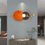 Horloge murale design en métal, formé par un cadran rond nordique de couleur orange avec 3 aiguilles et d'un second cadran rond marron avec la forme d'un cerf à l'intérieur, et une armature couleur or, horloge située dans une pièce à vivre