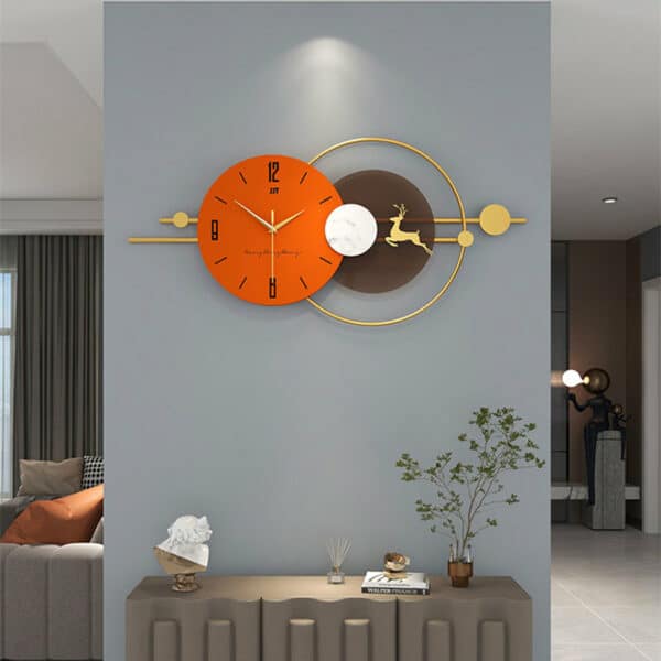 Horloge murale design en métal, formé par un cadran rond nordique de couleur orange avec 3 aiguilles et d'un second cadran rond marron avec la forme d'un cerf à l'intérieur, et une armature couleur or, horloge située dans une pièce à vivre