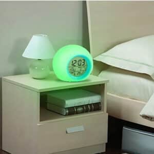Radio Réveil Enfant en Forme de Boule avec Rétroéclairage allumé en vert sur une table de nuit beige avec un lit à droite