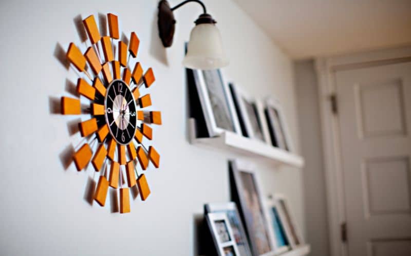Horloge très originale orange accrochée à un mur à côté d'étagère avec des livres et d'un luminaire.