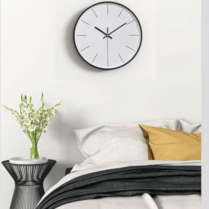 horloge murale ronde minimaliste design blanche avec tour noir au dessus d'un lit avec oreiller blanc et jaune