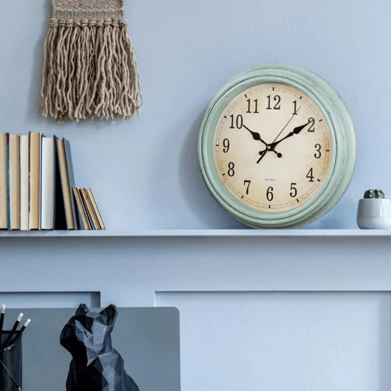 horloge murale ronde vintage silencieuse élégante verte sur fond gris bleu et posé sur une étagère bleue